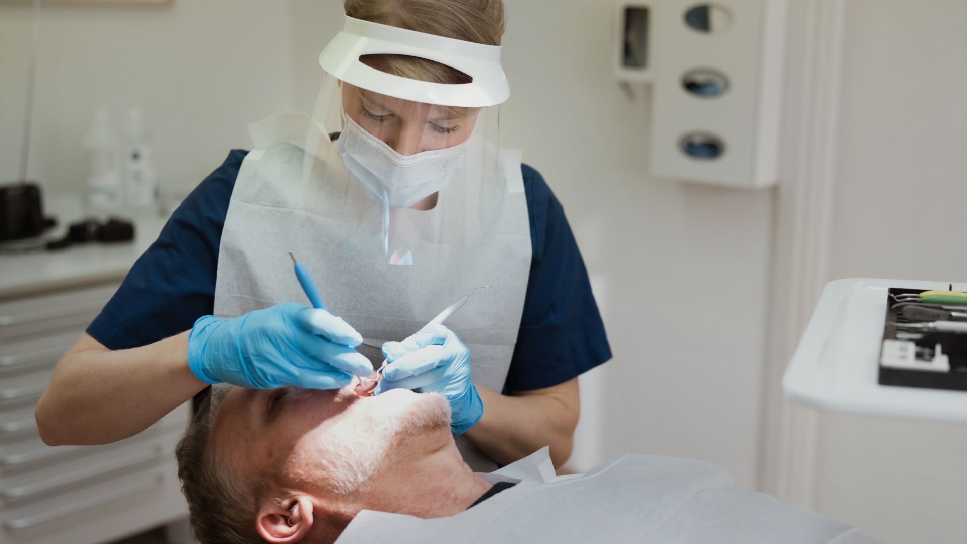 En tandläkare årjäng iförd skyddsutrustning utför en tandbehandling på en patient som ligger i en tandläkarstol, vilket borgar för trygg och professionell tandvård årjäng.