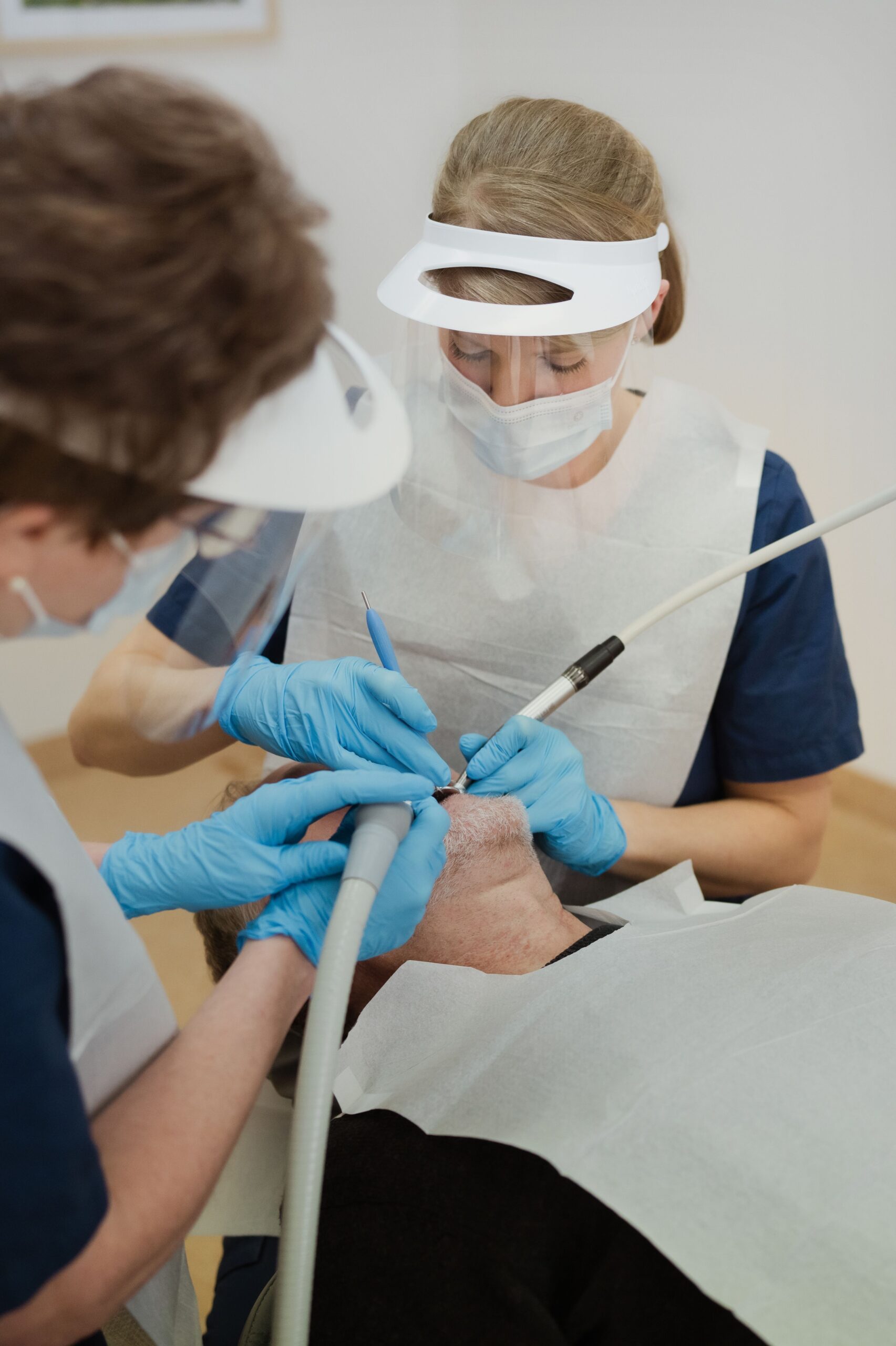 Två tandvårdspersonal iförda ansiktsskydd och handskar utför en tandbehandling på en patient i en tandläkarstol, vilket återspeglar tandvård Sveriges höga standard.