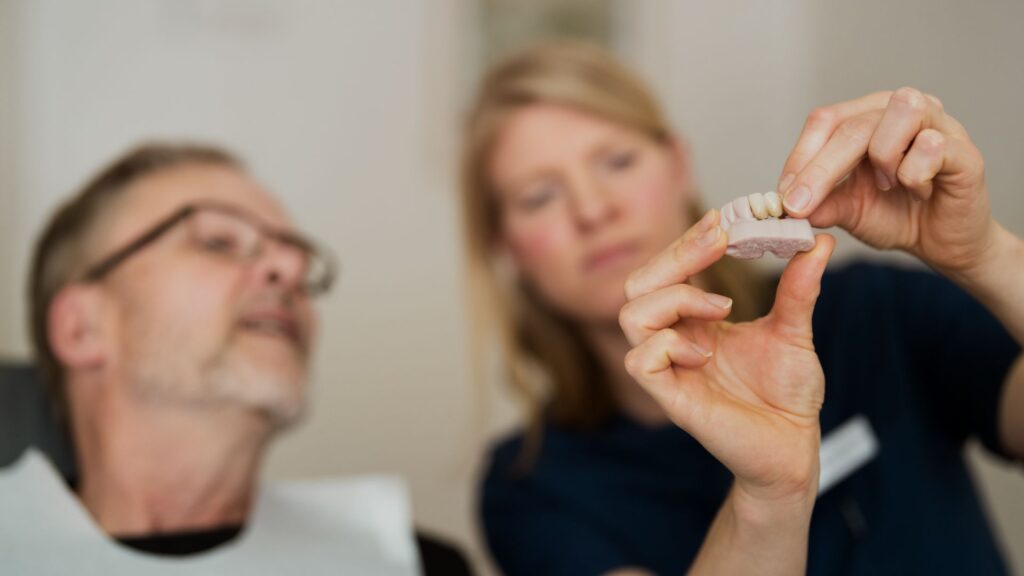 A tandläkare i Årjäng visar en patient en dental modell med tandimplantat under en konsultation.