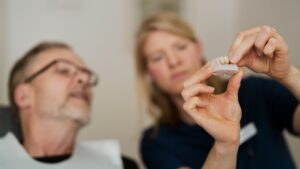 A tandläkare i Årjäng visar en patient en dental modell med tandimplantat under en konsultation.