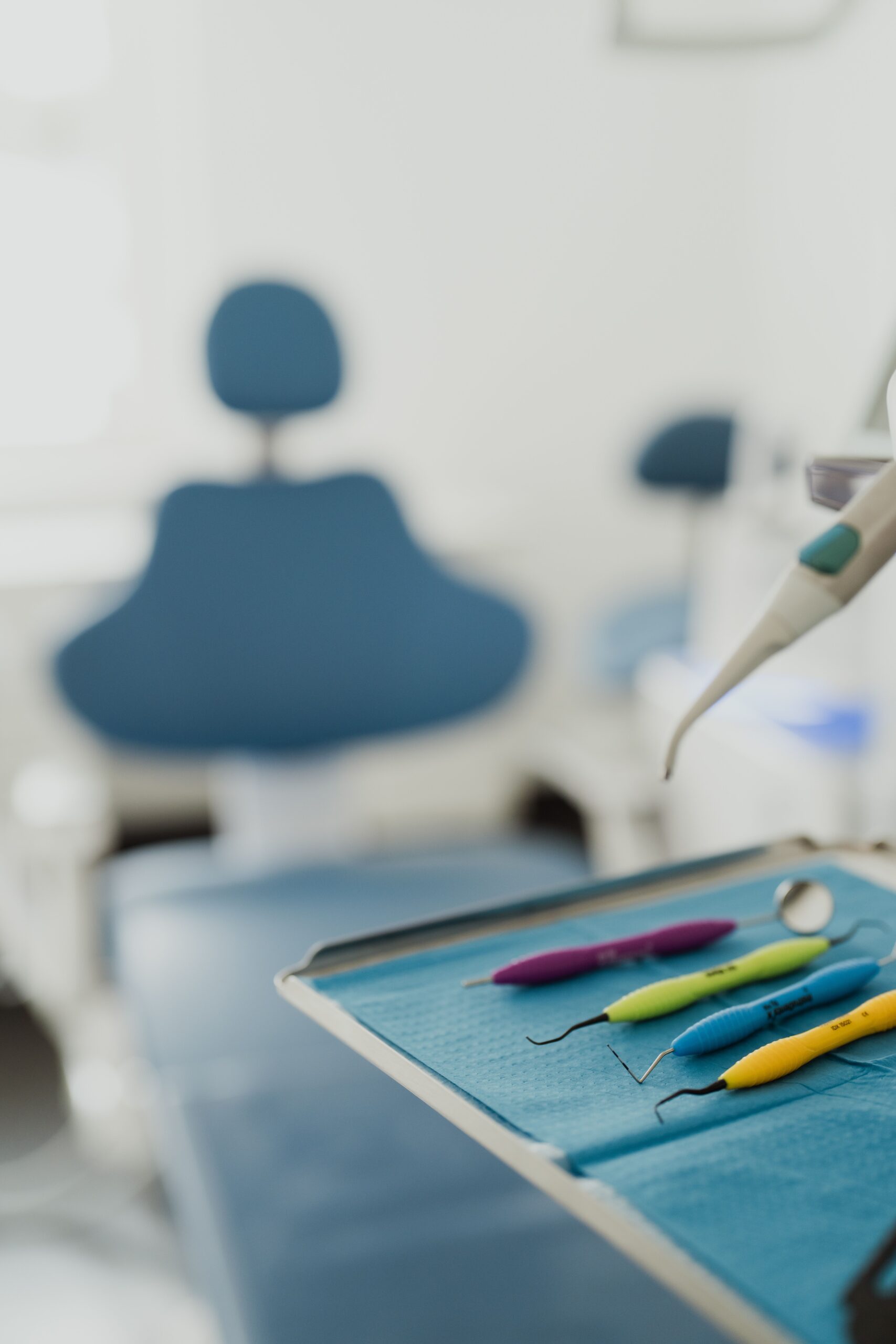 En bricka med tandläkarverktyg i förgrunden och en blå tandläkarstol i bakgrunden inne på en tandläkarklinik som specialiserat sig på tandimplantat, guidad av erfarna tandläkare Sverige.