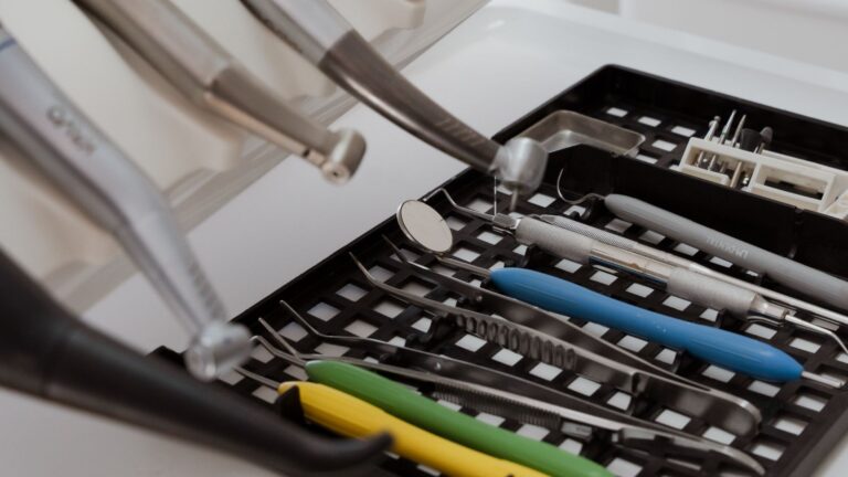 En bricka som innehåller olika tandläkarinstrument och verktyg, inklusive en munspegel, pincett och skalare med färgade handtag, som vanligtvis används av tandläkare Sverige för procedurer som implantat.