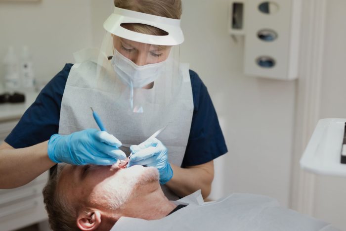 En tandläkare årjäng iförd skyddsutrustning utför en tandbehandling på en patient som ligger i en tandläkarstol, vilket borgar för trygg och professionell tandvård årjäng.