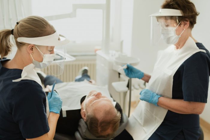 Två tandvårdspersonal i PPE tar hand om en patient som ligger i en tandläkarstol under en tandimplantatbehandling på en klinik inom Tandvård Sverige.
