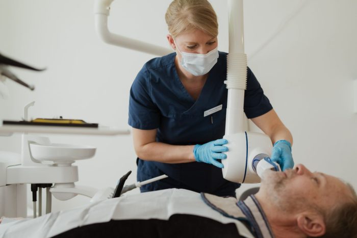 En tandläkare i operationskläder och mask placerar en röntgenapparat över en patients mun på en tandvårdsklinik och förbereder sig för en eventuell tandimplantatbehandling.