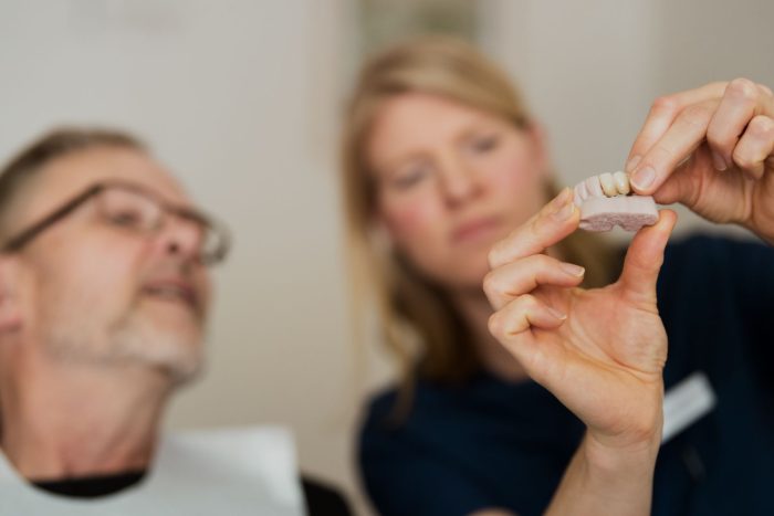 A tandläkare i Årjäng visar en patient en dental modell med tandimplantat under en konsultation.
