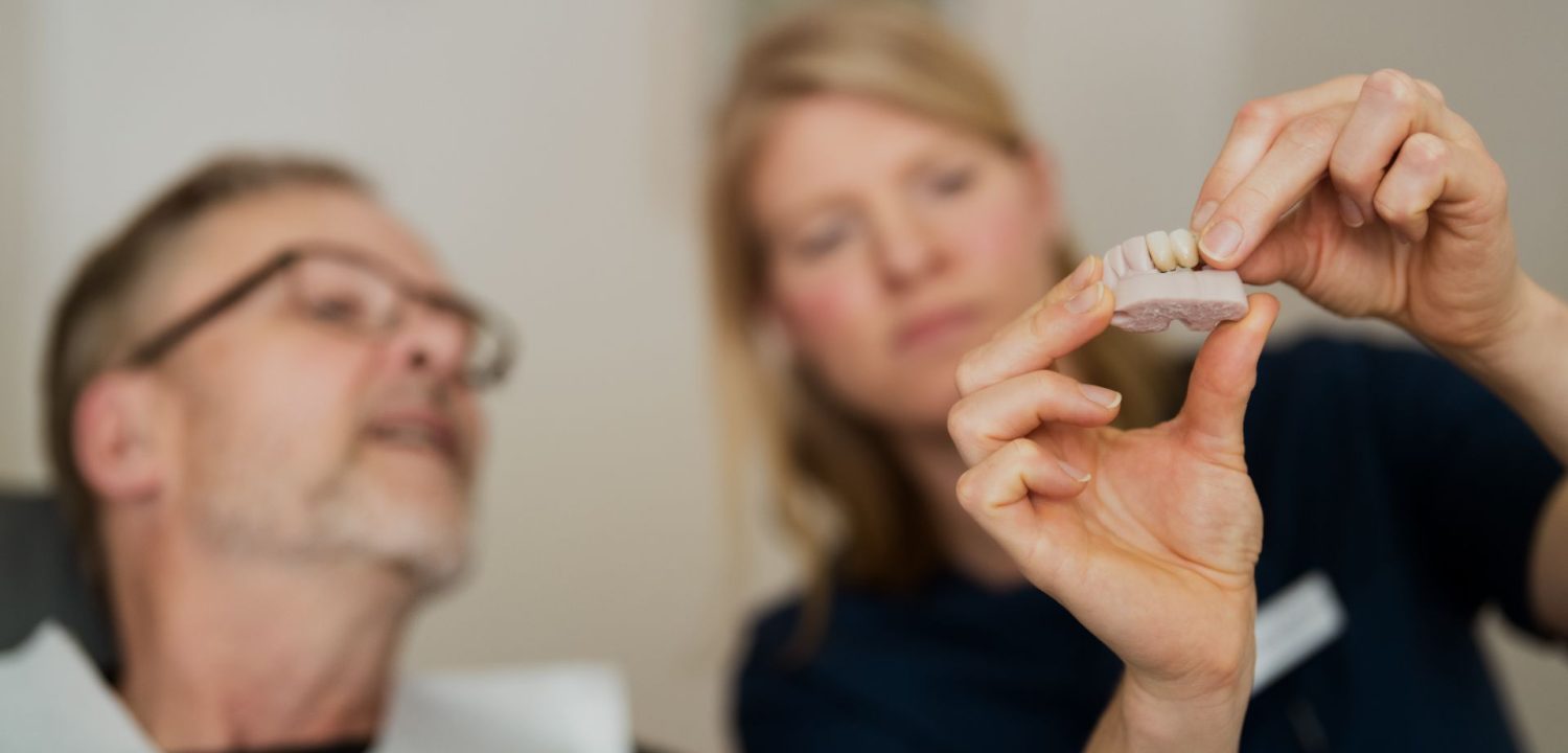 A tandläkare i Årjäng visar en patient en dental modell med tandimplantat under en konsultation.