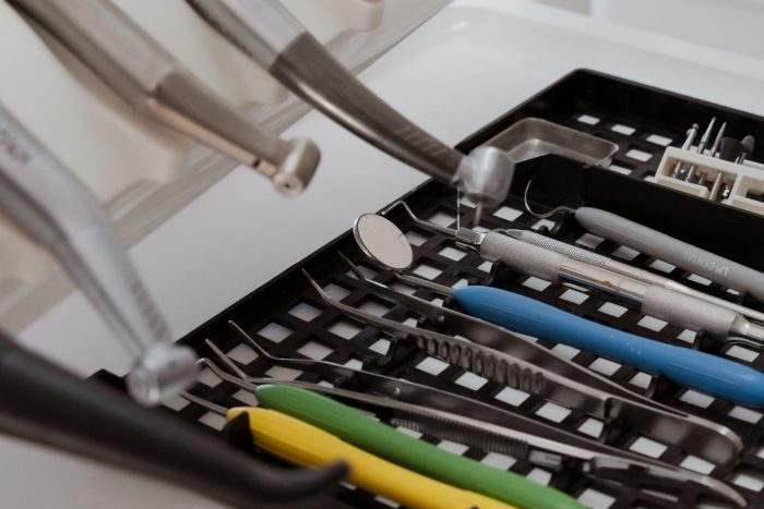 En bricka som innehåller olika tandläkarinstrument och verktyg, inklusive en munspegel, pincett och skalare med färgade handtag, som vanligtvis används av tandläkare Sverige för procedurer som implantat.